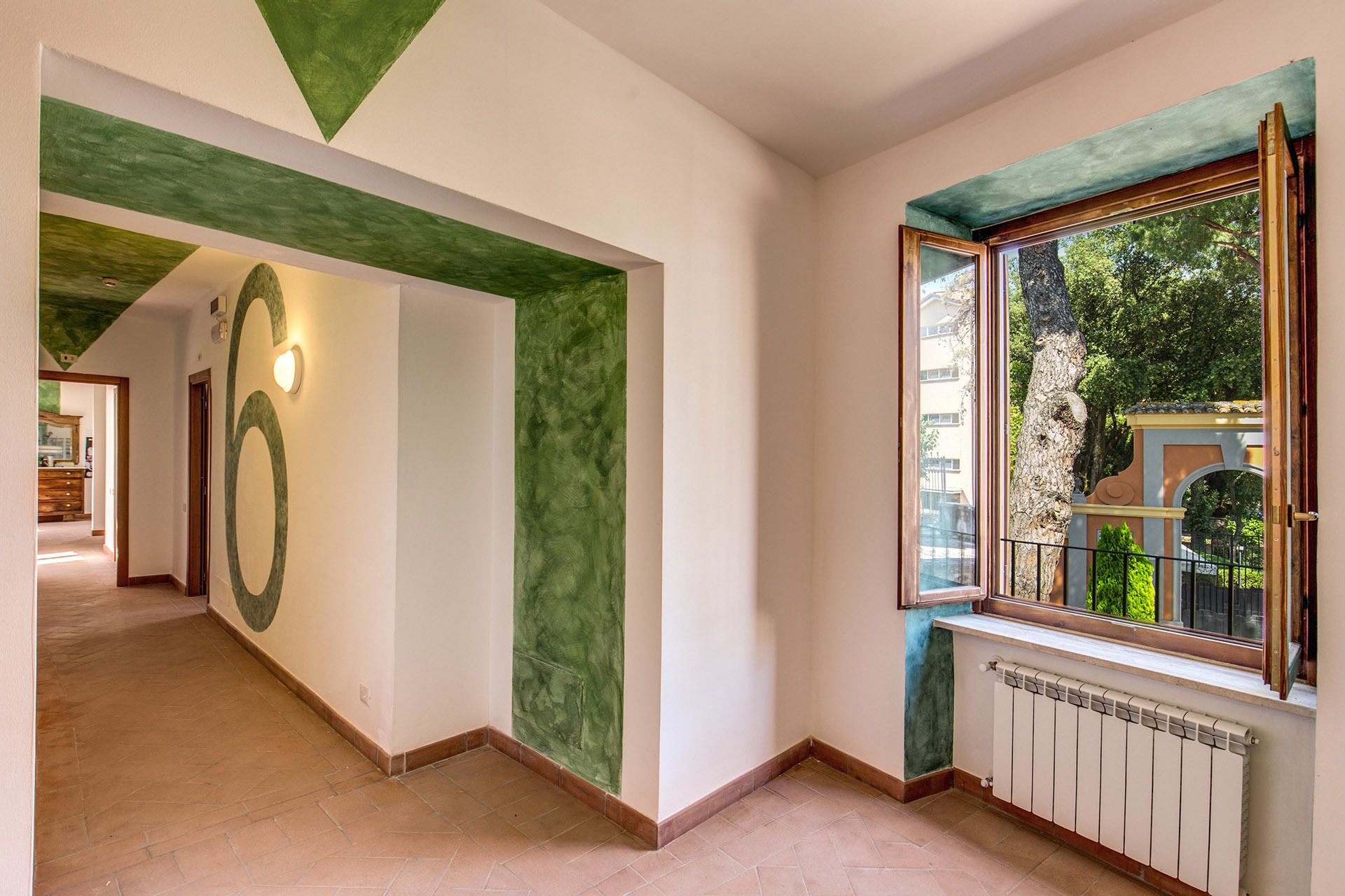 Um corredor com uma parede verde de destaque, um design circular grande e uma janela com vista para vegetação lá fora.