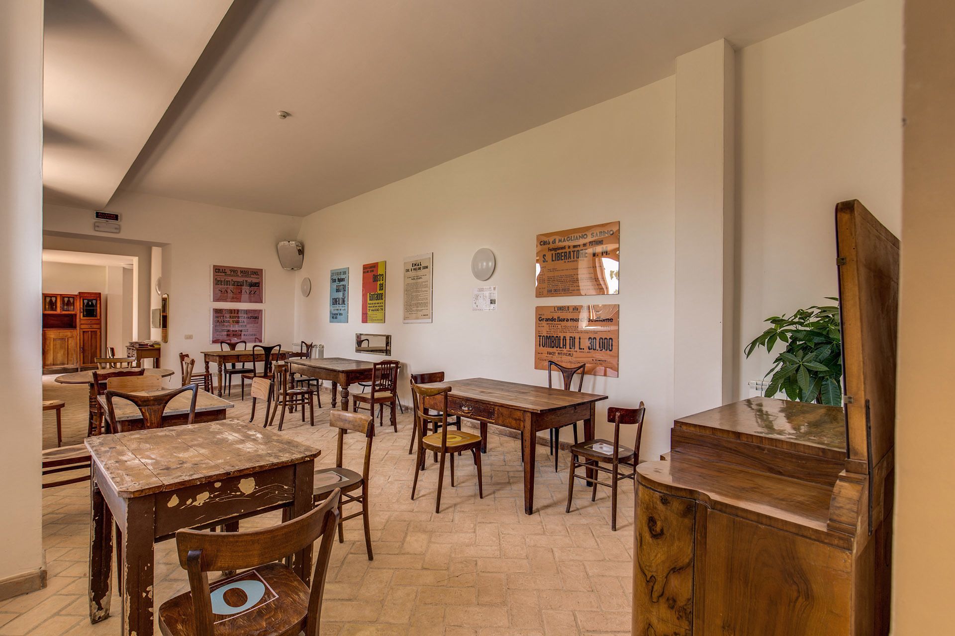 A dining area with wooden tables and chairs, a plant, and posters on the wall.