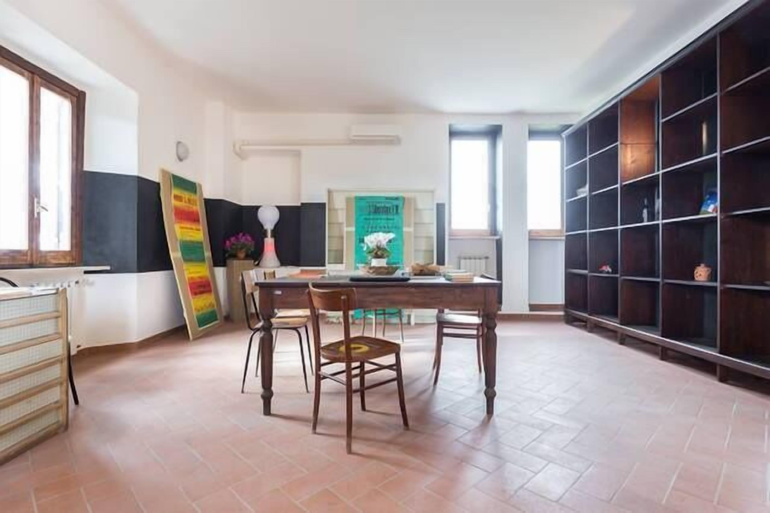 A dining area with a wooden table and chairs, a bookshelf, and a tiled floor.