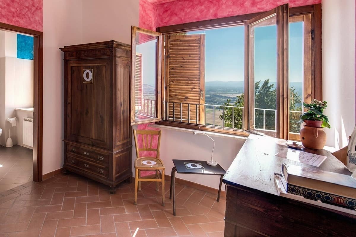 Une pièce comprenant un meuble en bois, une chaise, une table avec un ordinateur portable et une fenêtre donnant sur le paysage.