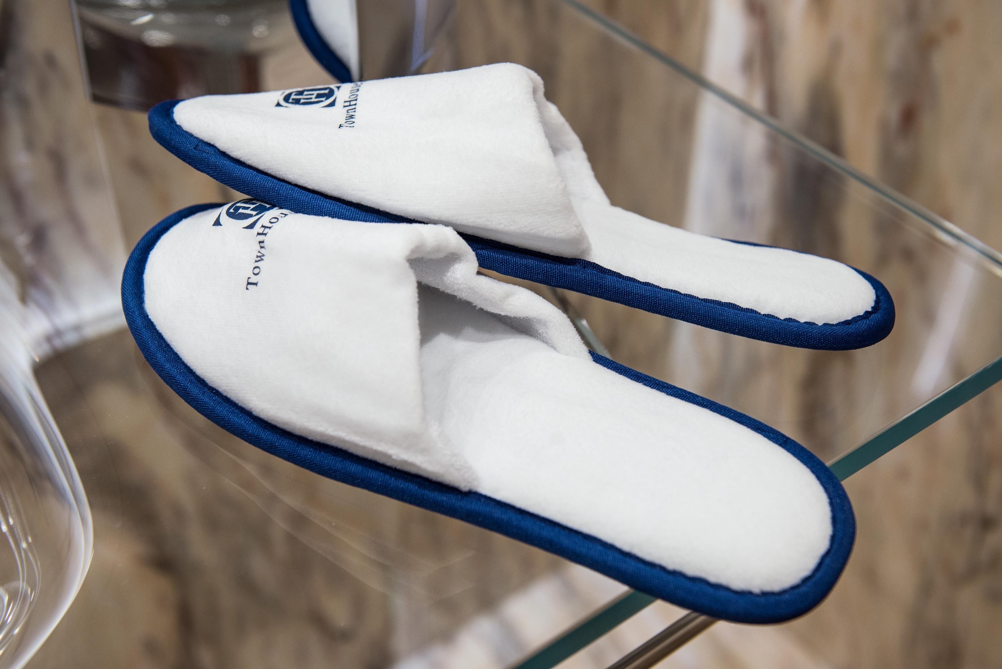 Un par de zapatillas blancas con detalles azules y un logotipo en la suela, sobre una superficie de vidrio transparente.