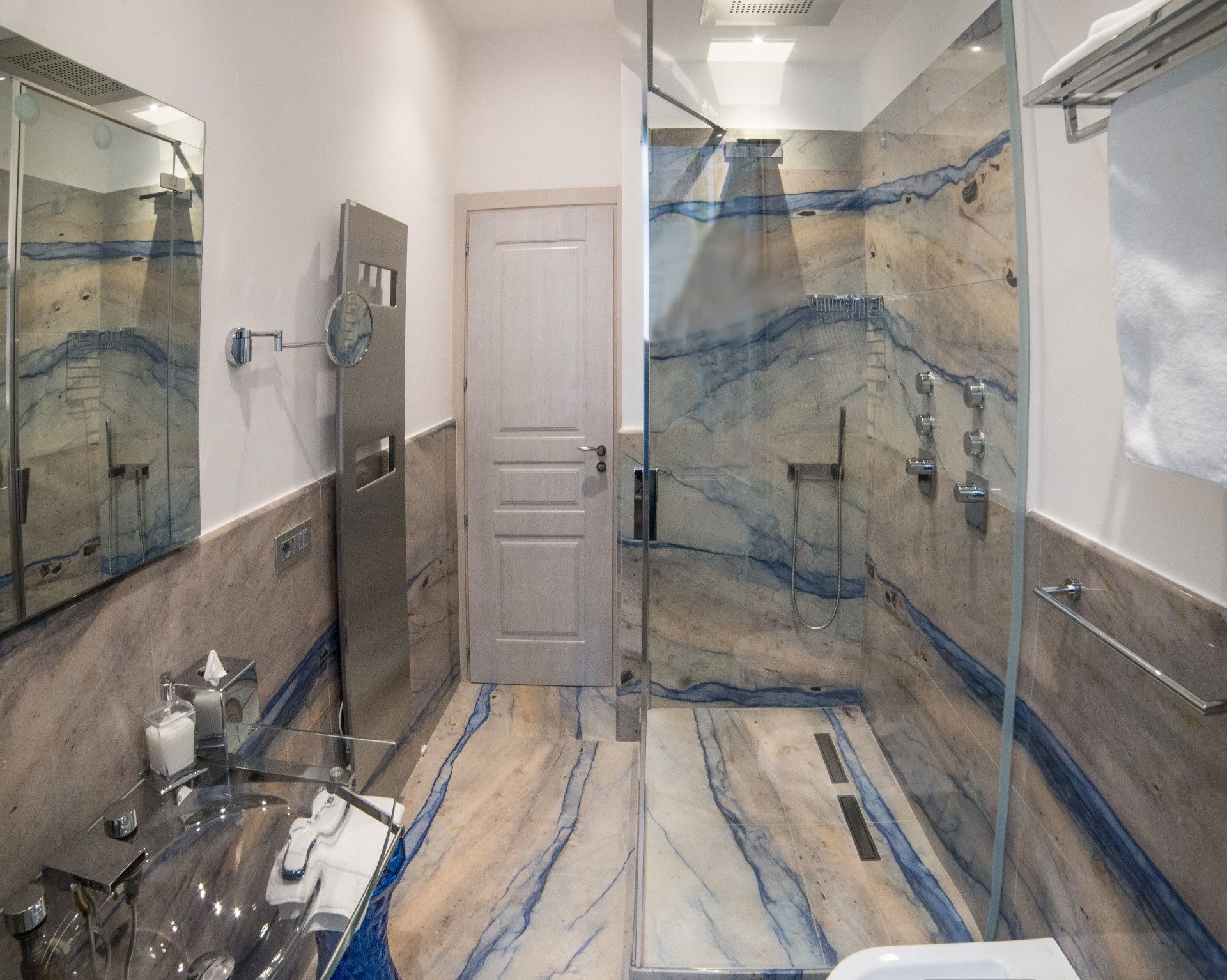 Une salle de bain moderne dotée d’une douche à parois de verre, d’un sol en marbre et d’un grand miroir.