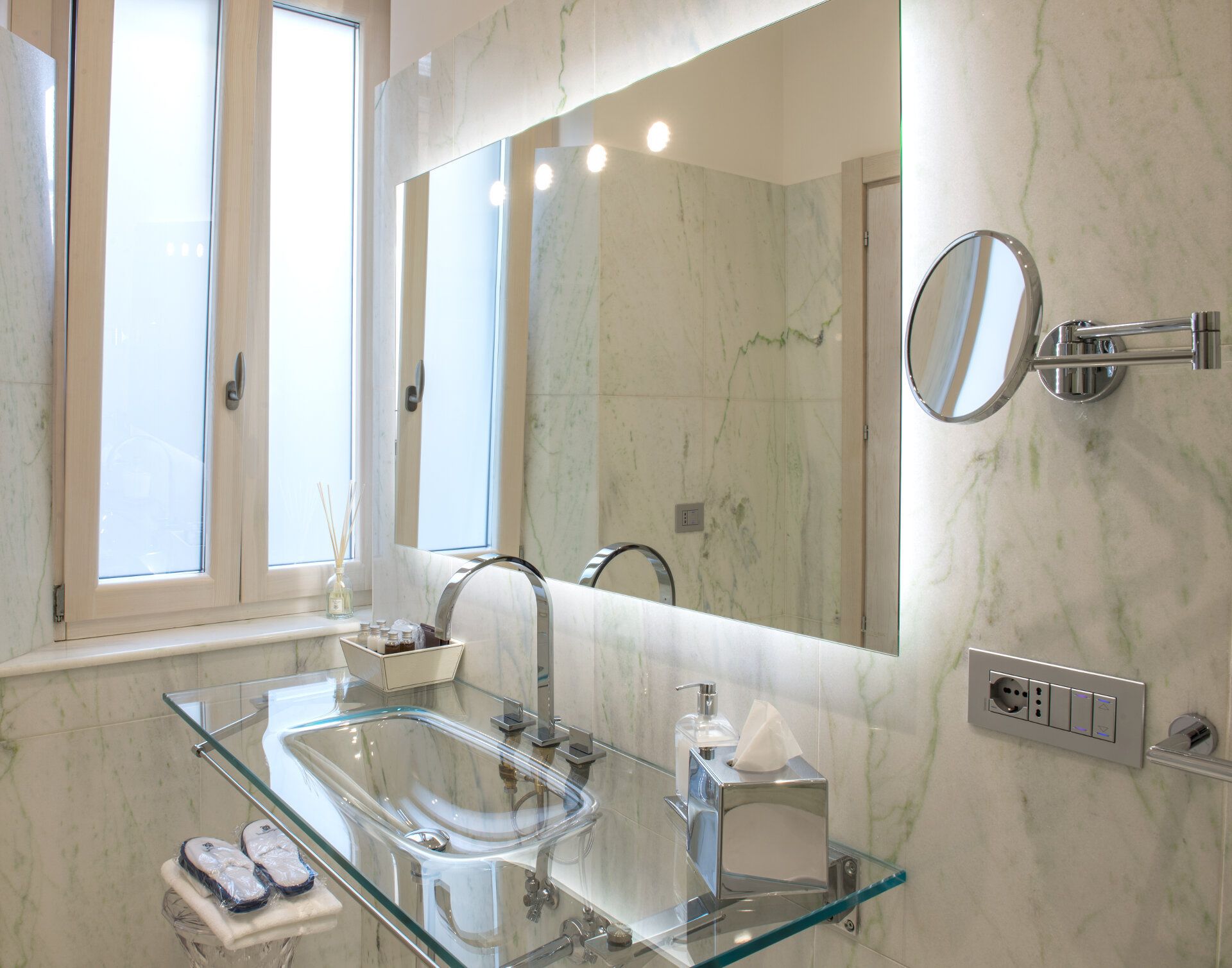 Un baño moderno con un lavabo de vidrio, un espejo grande y una ventana.