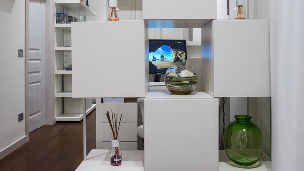 Un salon moderne doté d’un téléviseur à écran plat, d’étagères blanches et de diffuseurs d’arômes décoratifs en forme de roseaux.