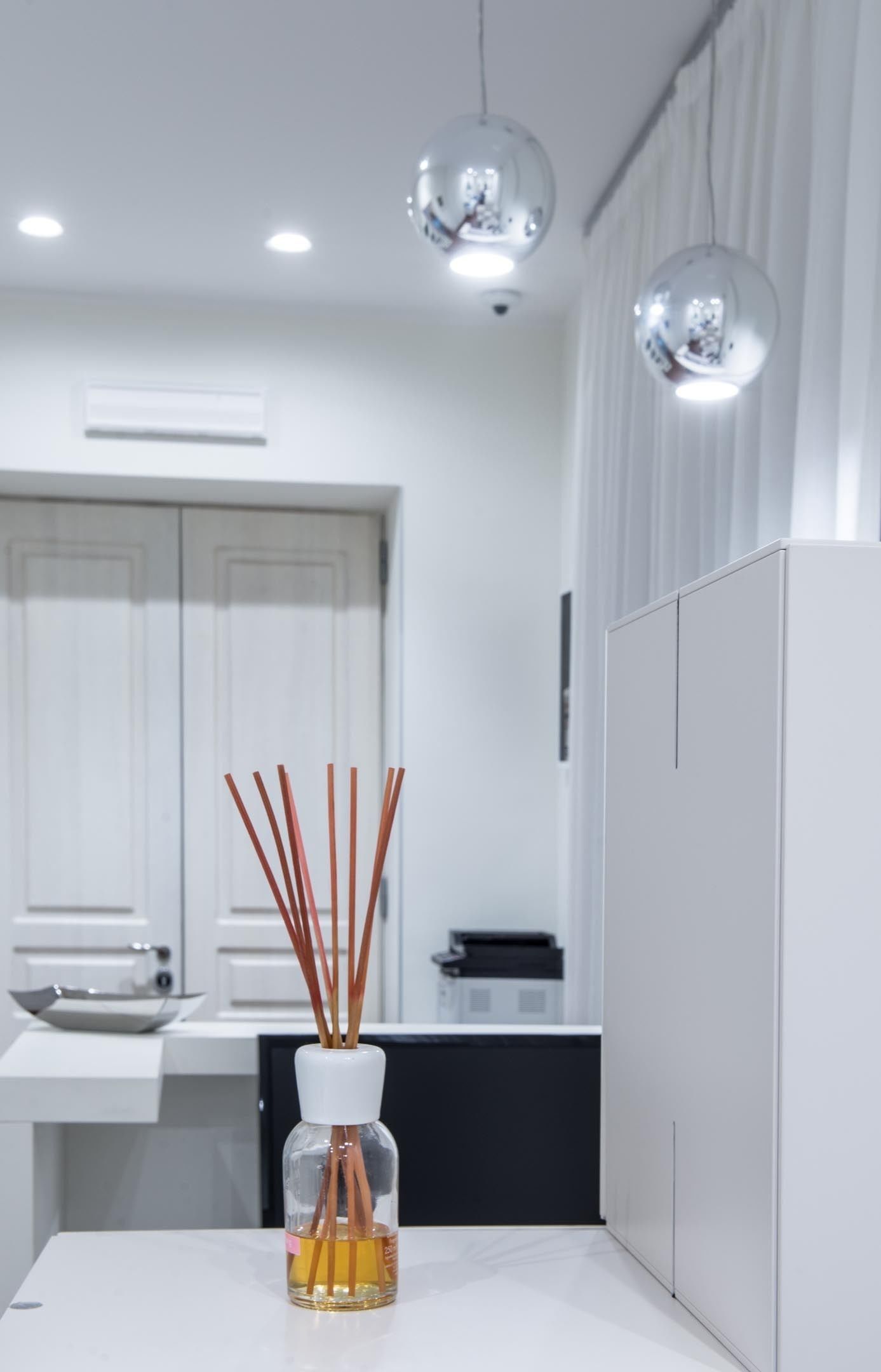 A modern kitchen with white cabinetry, a white countertop, and a vase with reed sticks.