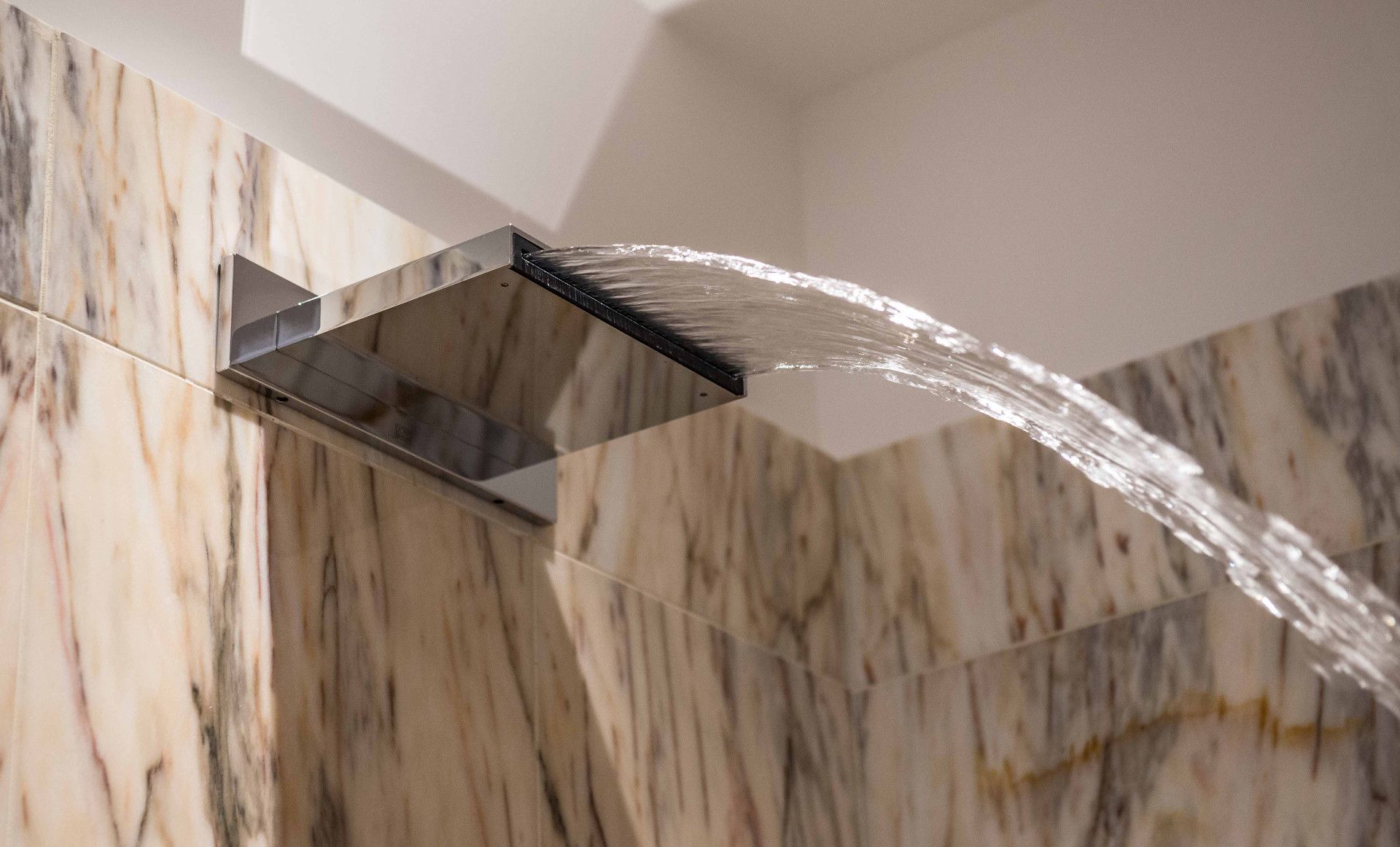 Une salle de bain moderne avec un mur en marbre et un robinet élégant au fini métallique.