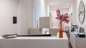 Un espace d’accueil moderne, au design minimaliste, comprenant un comptoir d’accueil, un vase avec des fleurs roses et un grand miroir mural.