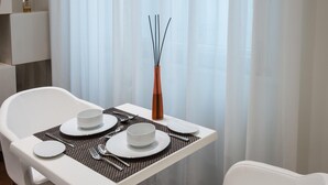 Une table à manger dressée avec de l’assiette, des bols et des couverts blancs, agrémentée d’un vase contenant des branches noires et d’une bougie.