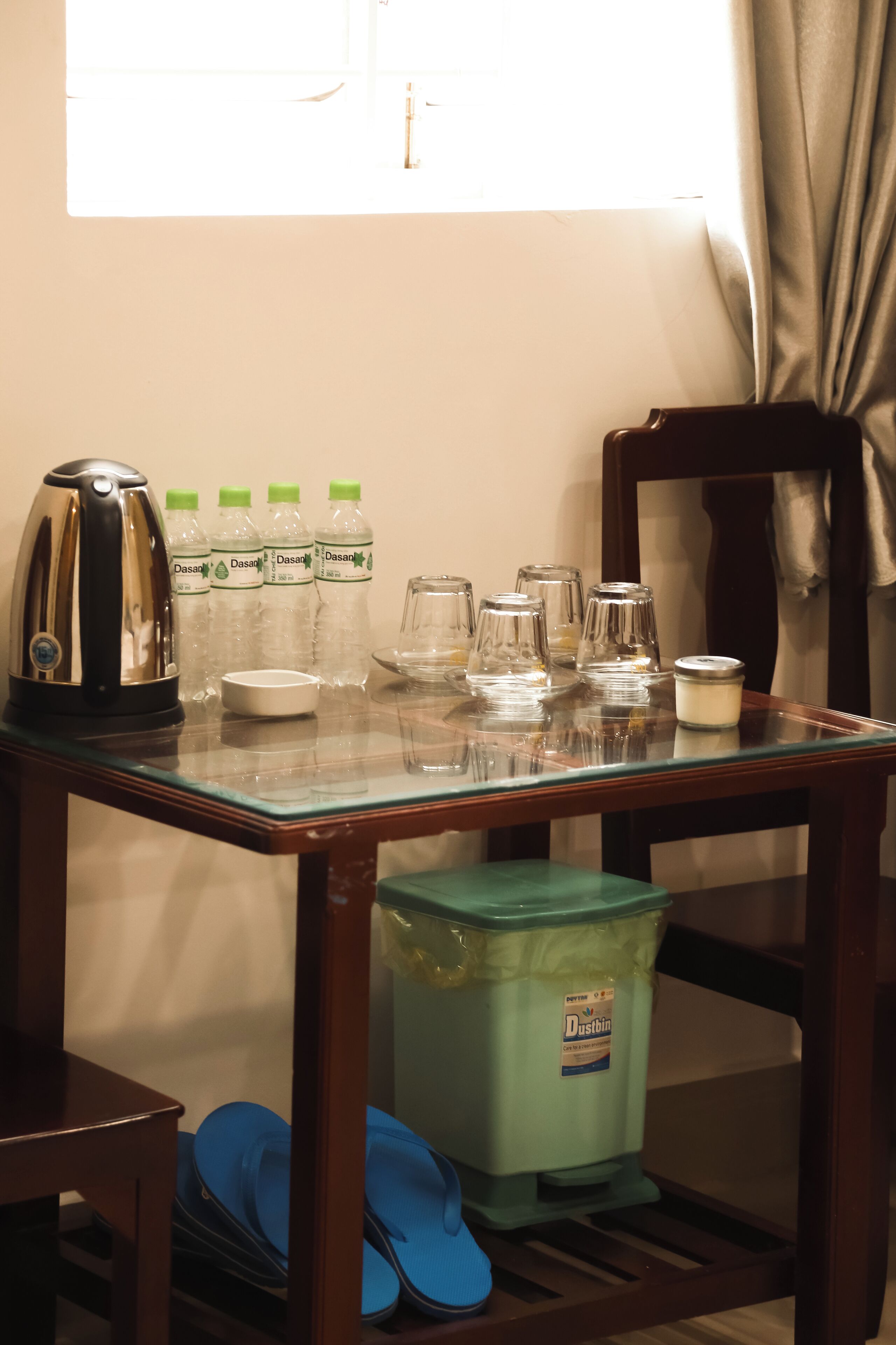 A room with a table set for breakfast, including a kettle, Dasani water bottles, and glassware.