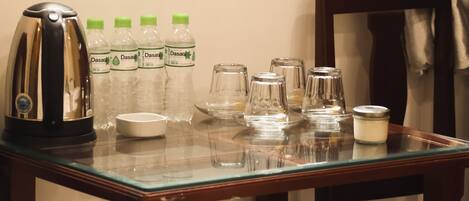A room with a table set for breakfast, including a kettle, Dasani water bottles, and glassware.