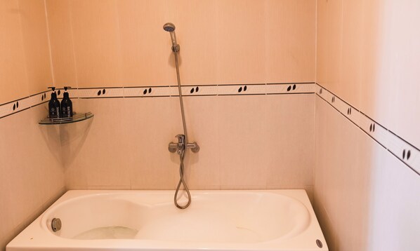 Un baño con bañera, ducha y un estante con artículos de aseo.