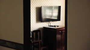 A room with a television mounted on the wall, a wooden cabinet, and a chair.