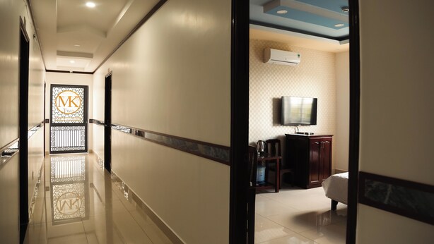 A hotel corridor with a reflective floor, a decorative gate with a logo, a television, and a bed in a room.
