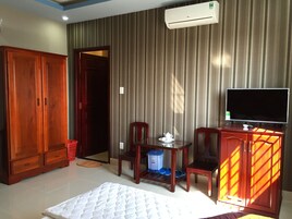 Una habitación de hotel con cama, televisión, armario de madera, una mesita con una silla y ventana con cortinas.