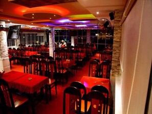A restaurant with multiple tables and chairs, a stone wall, and a stage area. - Minh Kieu Hotel (My Tho)