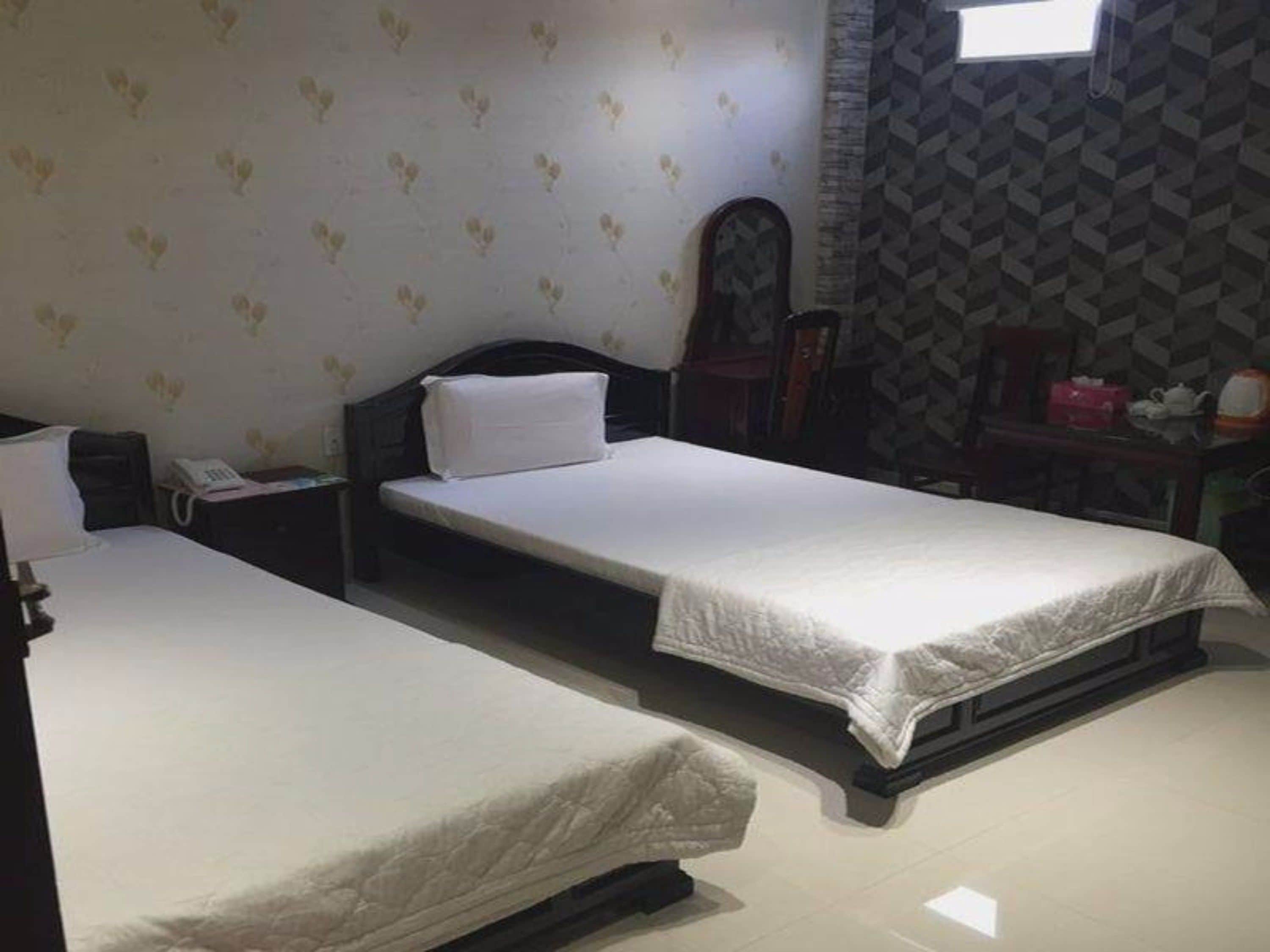 A hotel room with two single beds, a nightstand with a phone, and a patterned wall.