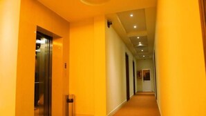 A corridor with a carpeted floor, a trash bin, and a door leading to an elevator. - Minh Kieu Hotel (My Tho)