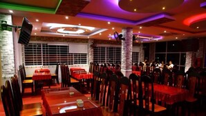 A restaurant with multiple tables and chairs, a stage for live performances, and a modern ceiling design. - Minh Kieu Hotel (My Tho)