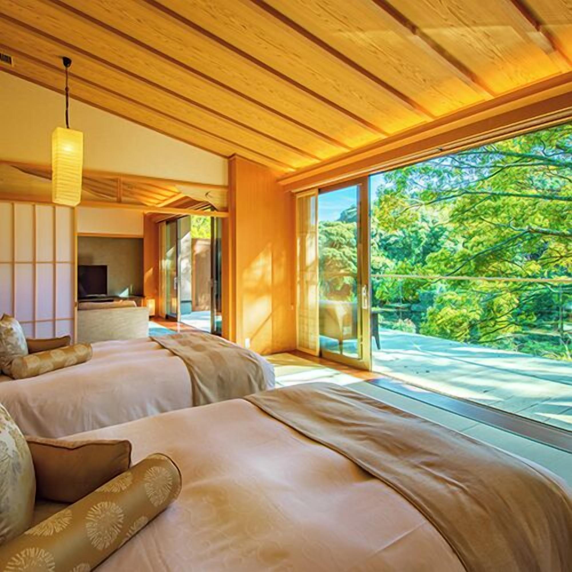 A bedroom with two beds, a television, and a large sliding glass door leading to a balcony with a view of trees.