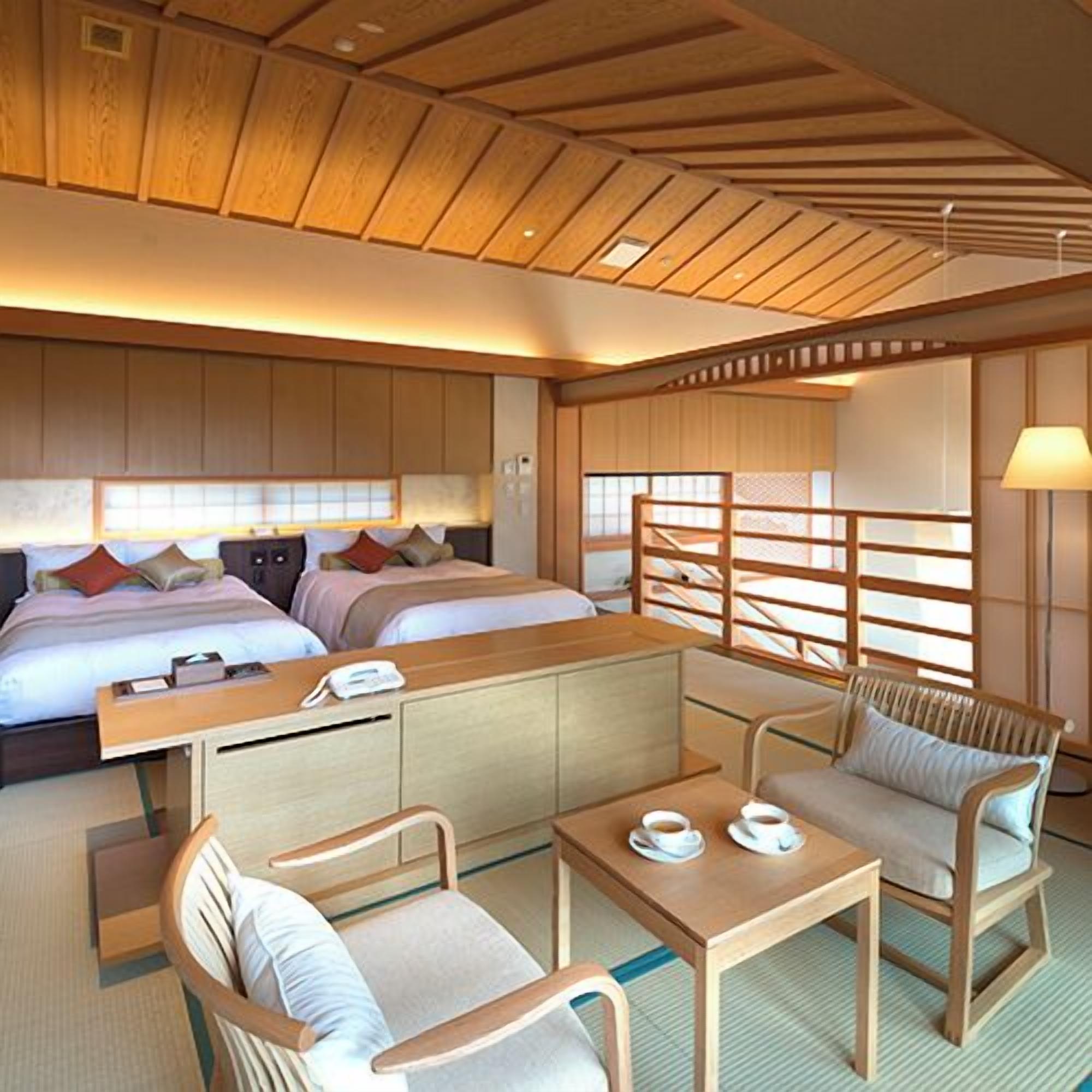 A hotel room with a bed, bedside tables, a desk, chairs, and a view through a window.