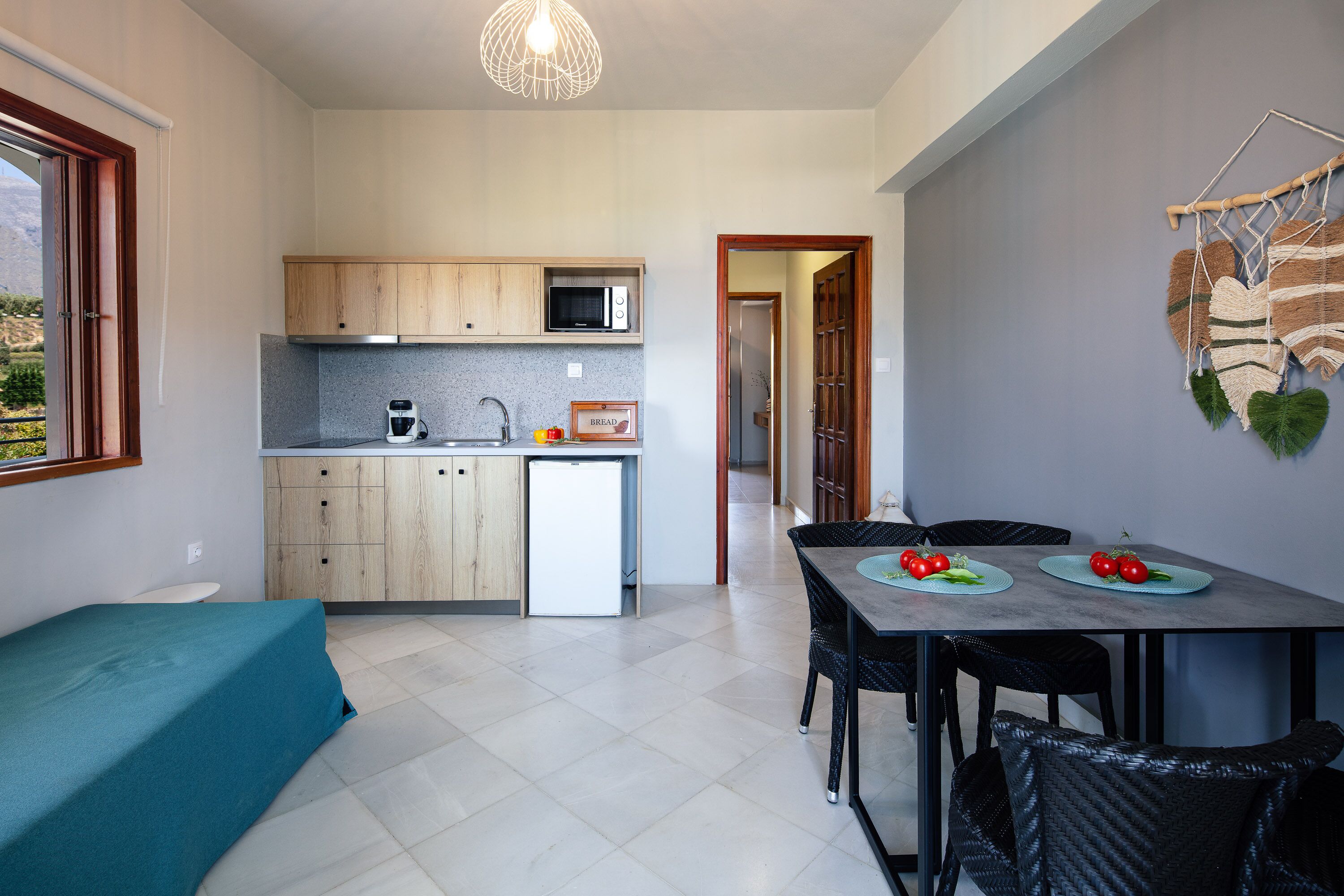 A compact kitchen with wooden cabinets, a microwave, and a small refrigerator. There is a dining table with chairs and a blue tablecloth.