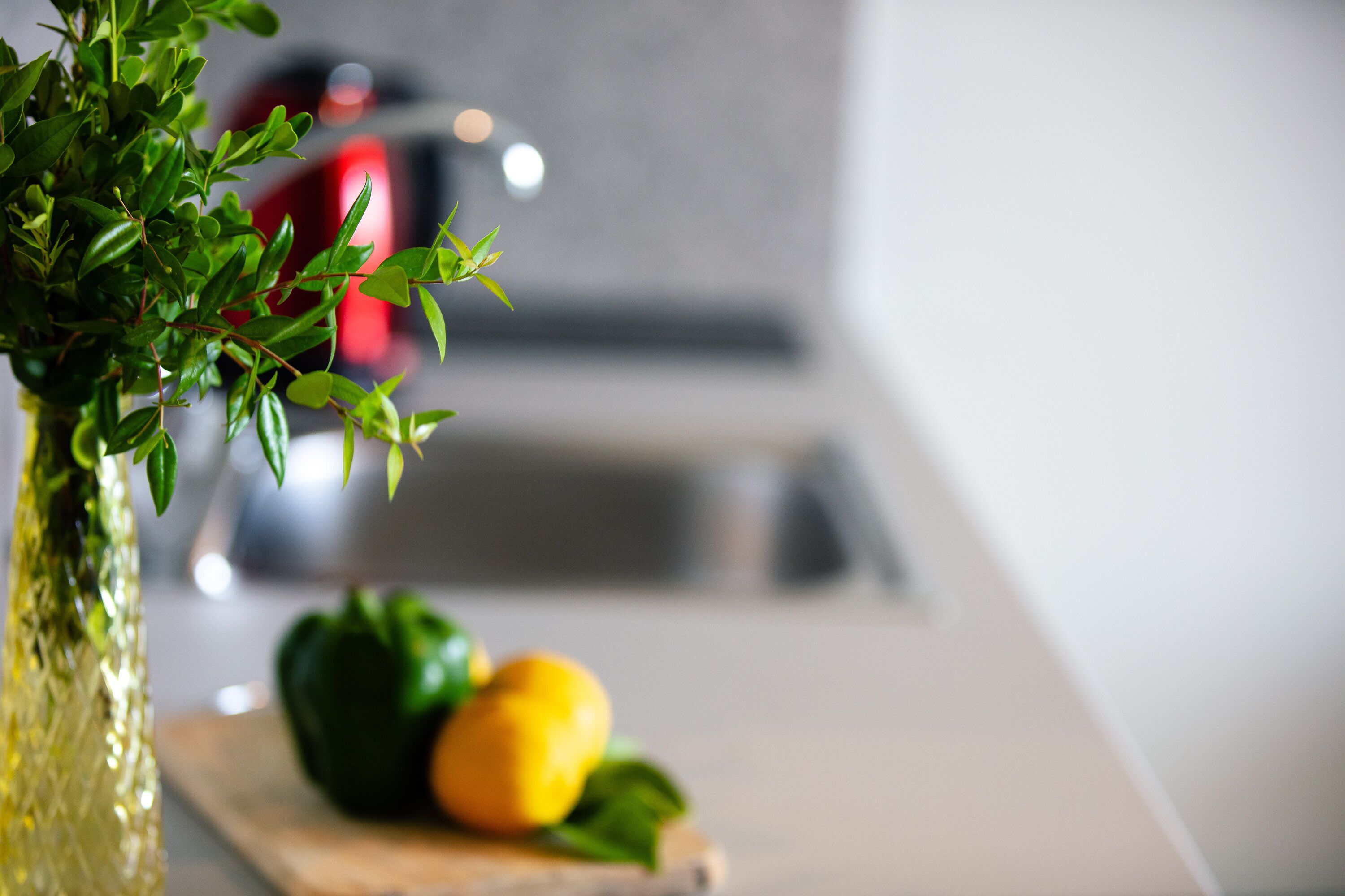 A kitchen counter with a potted plant, a green bell pepper, and a lemon on a cutting board.