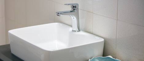 A white rectangular bathroom sink with a chrome faucet, a decorative shell-shaped bowl, and two small bottles of soap on a dark countertop.