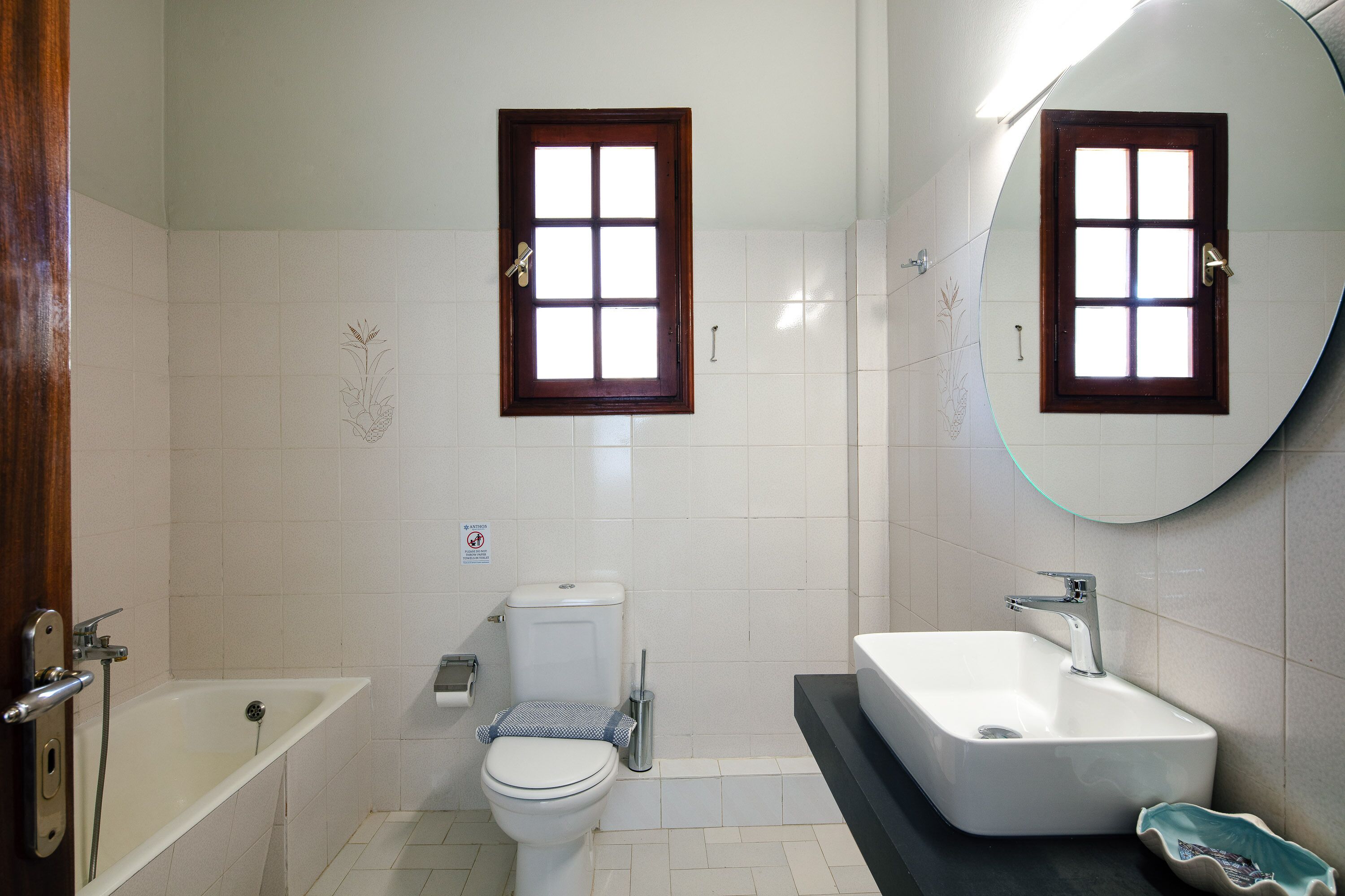 A bathroom with a bathtub, toilet, sink, and two windows.