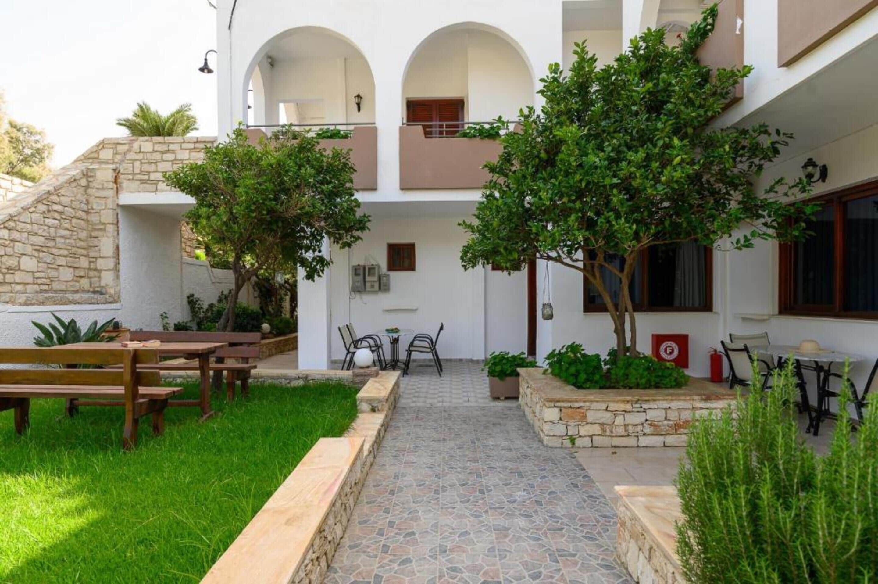 Un patio con bancos de piedra, un camino empedrado y plantas en macetas.