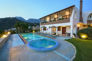 Relax by the pool with a hot tub at the center, surrounded by lush greenery and majestic mountains.
