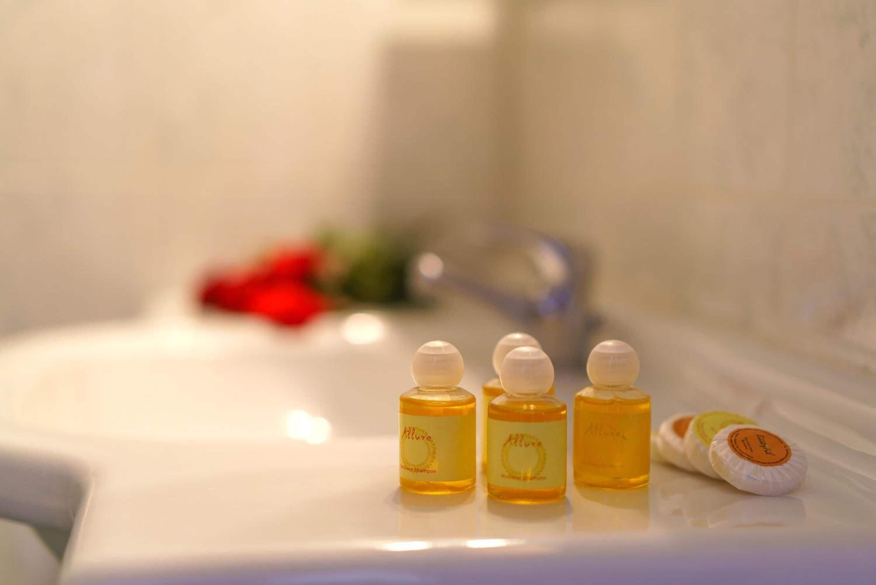 Un baño con un lavamanos blanco y tres botellas de champú sobre el mostrador.