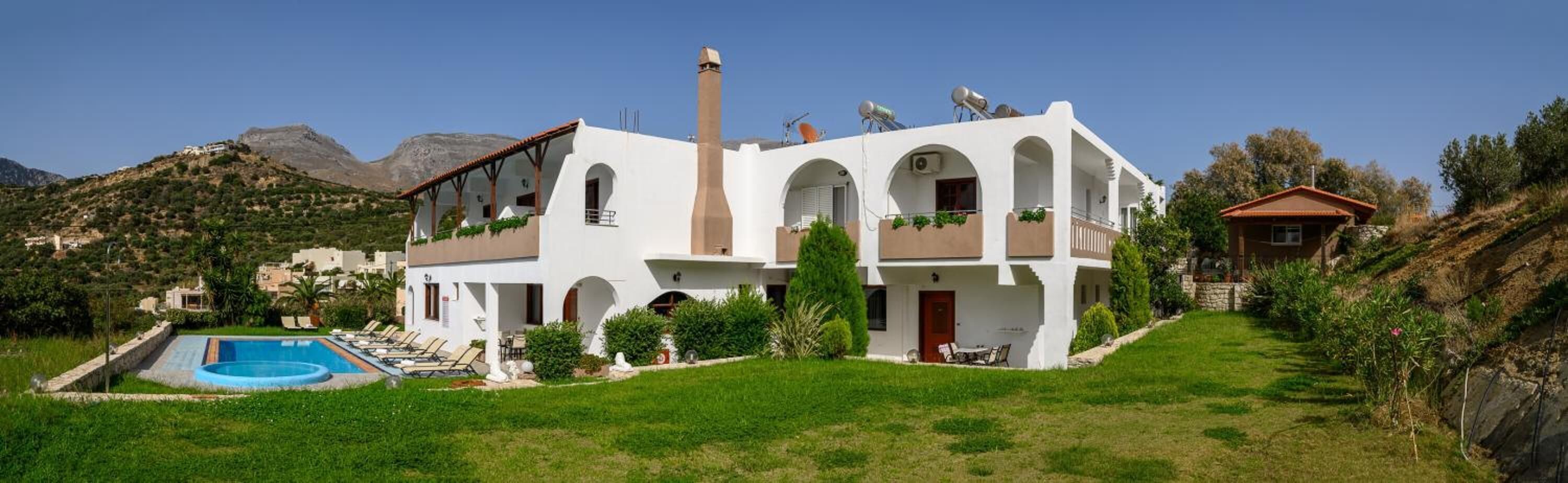 Une maison à deux étages avec une piscine, entourée de verdure et de montagnes.