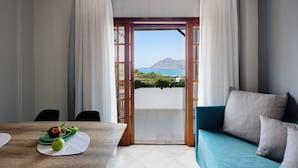 Una habitación con una mesa de comedor, un plato verde con una manzana y vista al mar a través de una puerta abierta.