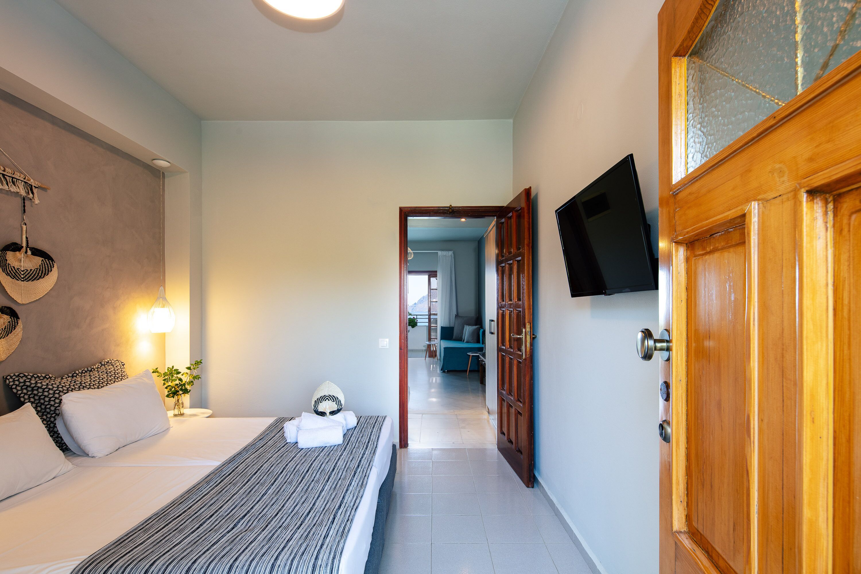 Een hotelkamer met een bed, nachtkastje, lamp en een aan de muur bevestigde televisie.