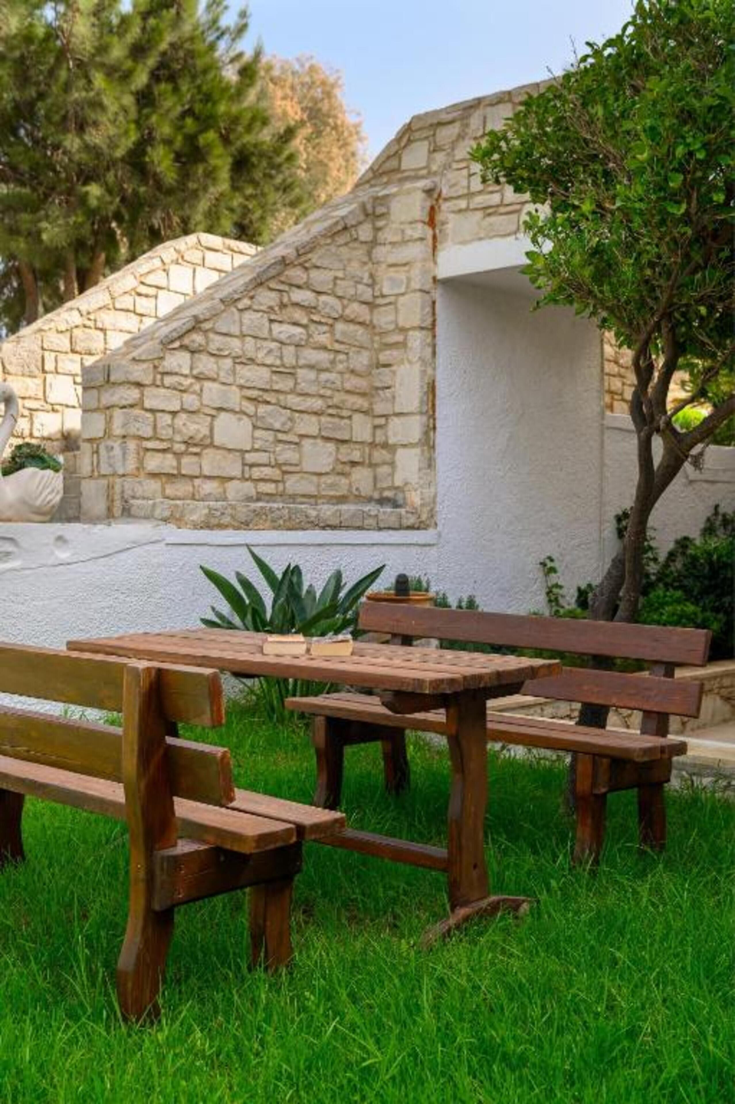 A stone wall with a white building, wooden benches, and a tree.