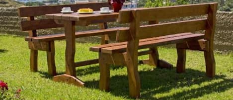 Un banco y una mesa de madera en un césped con montañas al fondo.