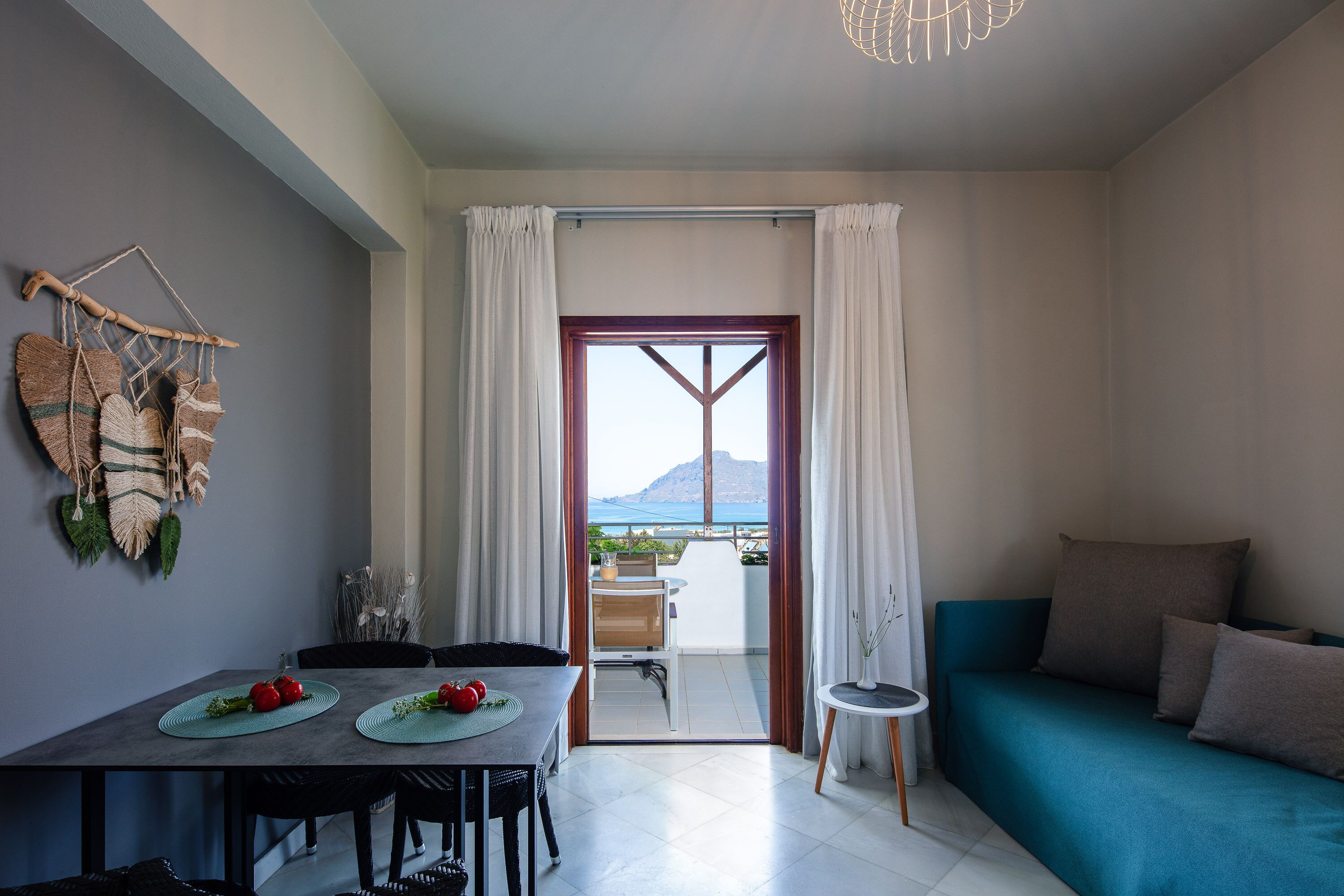 Una sala de estar moderna con sofá, una mesa de comedor con individuales y vista al mar a través de un gran ventanal.