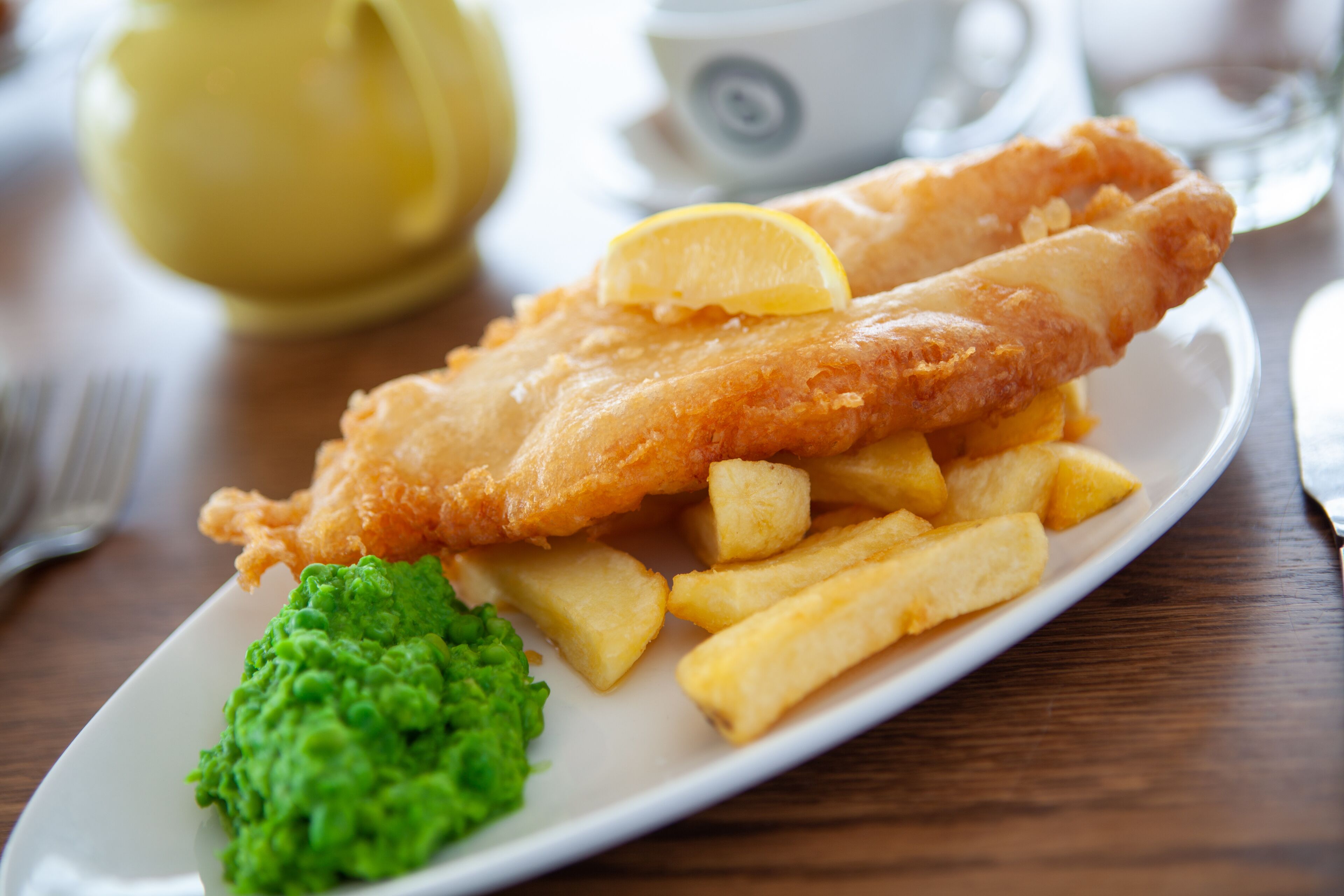 A plate of fish and chips with a lemon wedge and mushy peas.