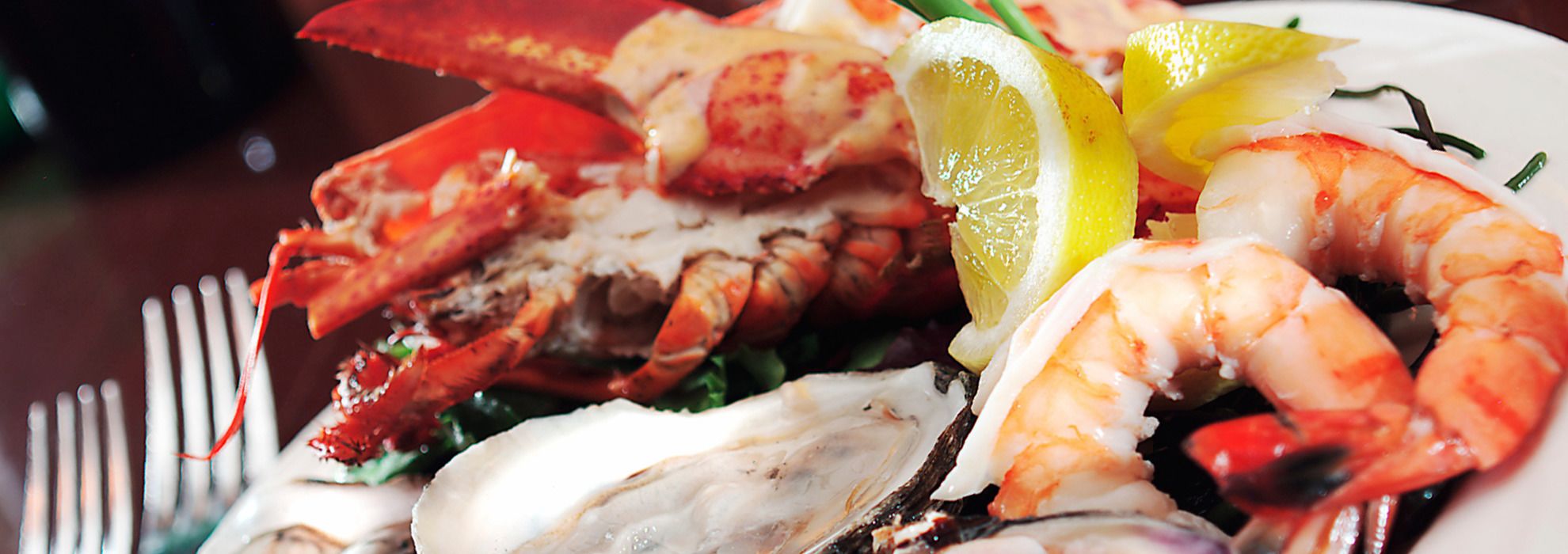 Un plateau de fruits de mer comprenant du homard, des crevettes et des huîtres, agrémenté de rondelles de citron.