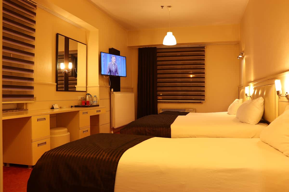 A hotel room with two beds, a desk, a television, and a large mirror.