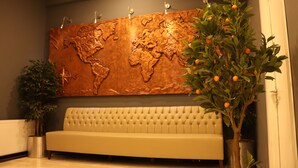 Un hall con un mural de un mapa mundial, un sofá, una planta en maceta y un pequeño árbol con naranjas.