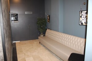 Un espace d’accueil avec un canapé beige, une plante en pot et un panneau indiquant l’emplacement d’une consigne à bagages.