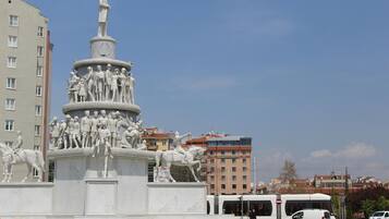 A large white monument with multiple figures, surrounded by buildings and a bus.