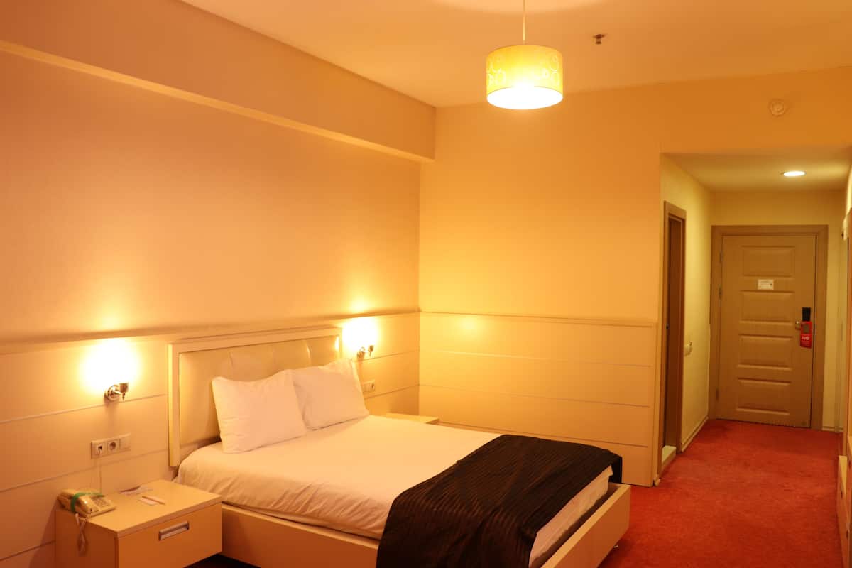 A hotel room with a bed, bedside table, lamp, and a door leading to another room.