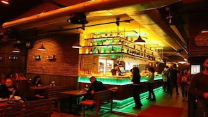 Una zona de bar con mobiliario de madera y una barra iluminada en verde.