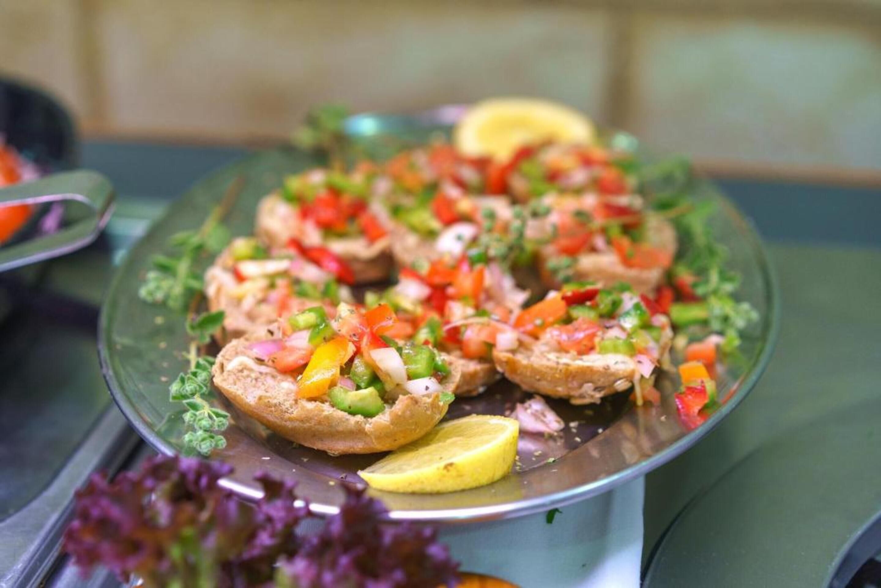 Een schaal open belegde sandwiches met diverse toppings, versierd met kruiden en een citroenpartje.