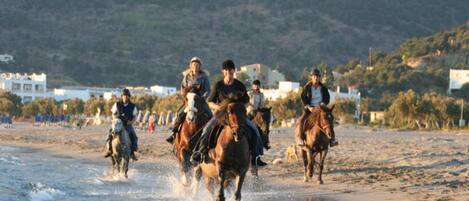 A beach scene with people riding horses along the shoreline.