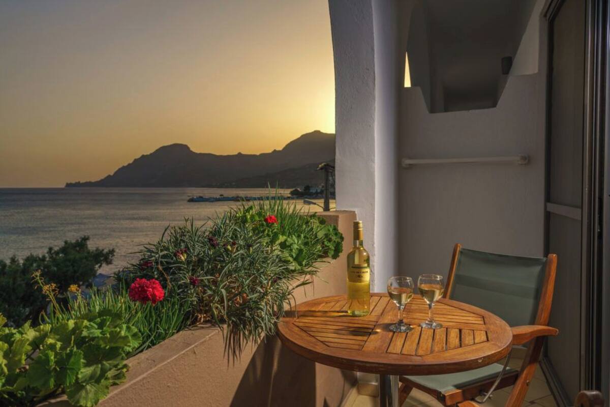 A wooden table with a bottle and glasses on a balcony overlooking the sea.