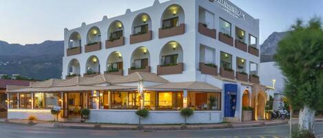A hotel with a white facade, multiple balconies, and a covered outdoor seating area.
