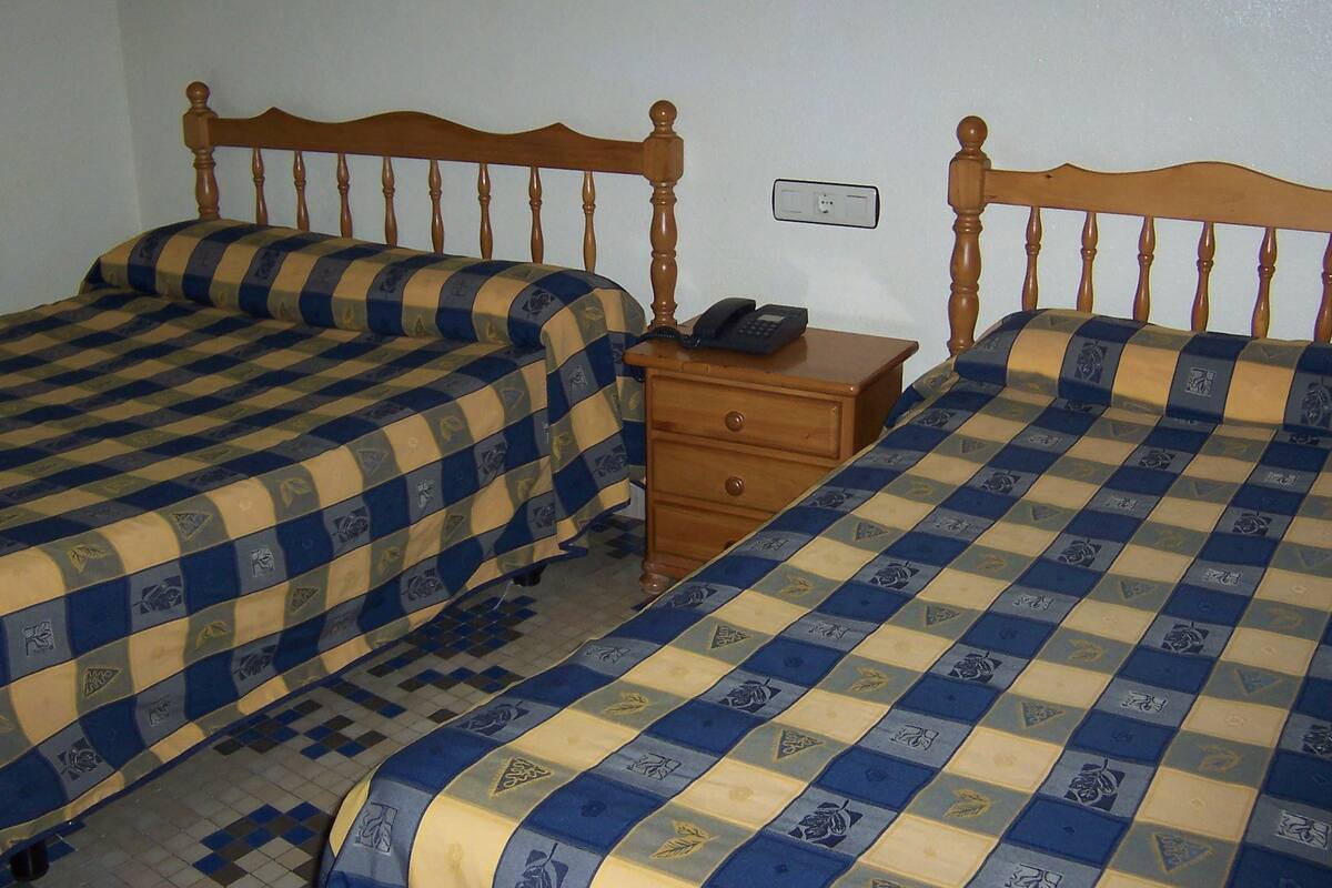 Un dormitorio con dos camas, cada una con una colcha a cuadros, un cabecero de madera y una mesita de noche con teléfono.